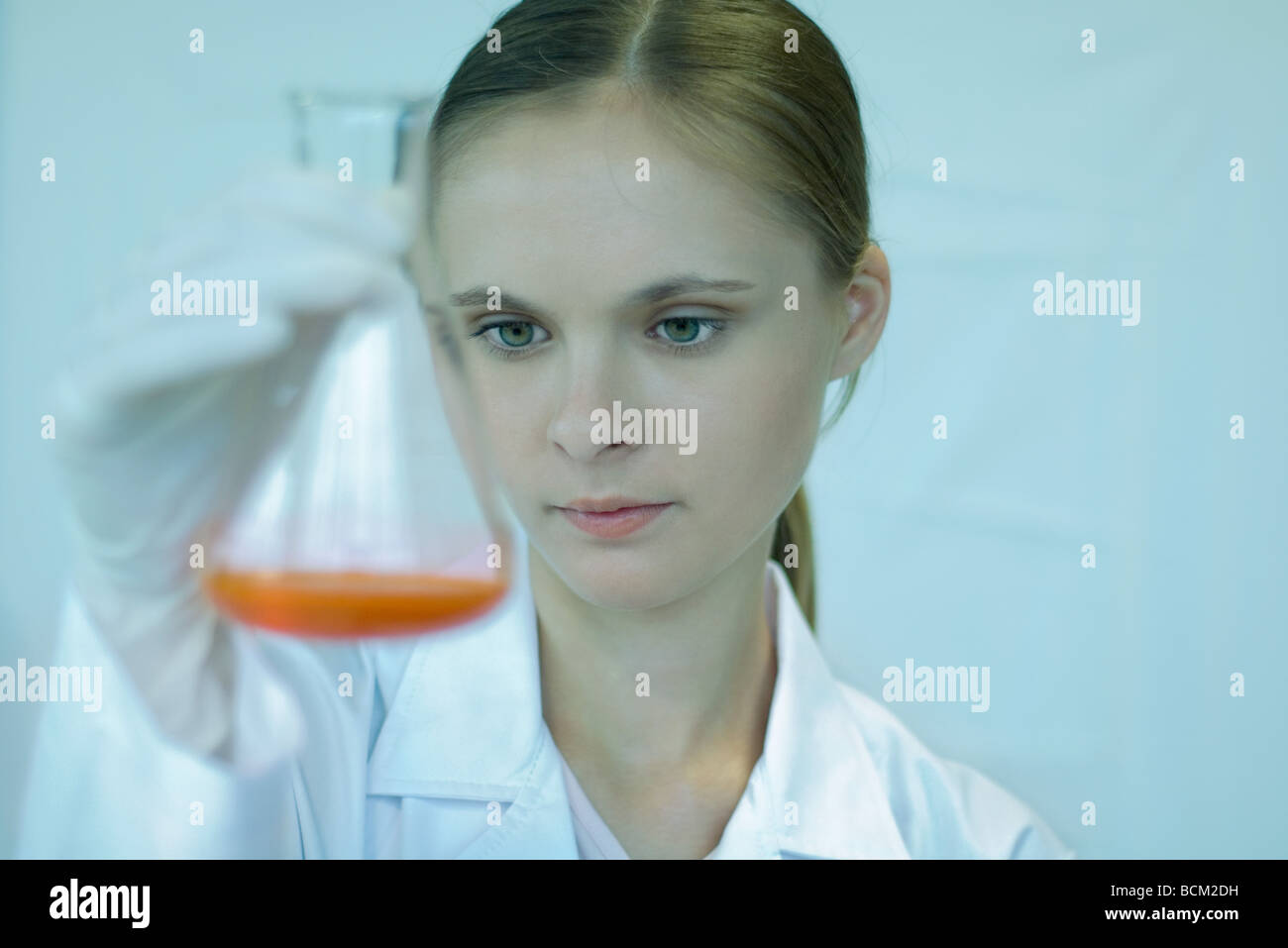 Female scientist holding up bécher avec liquide à l'intérieur, regardant vers le bas, close-up Banque D'Images