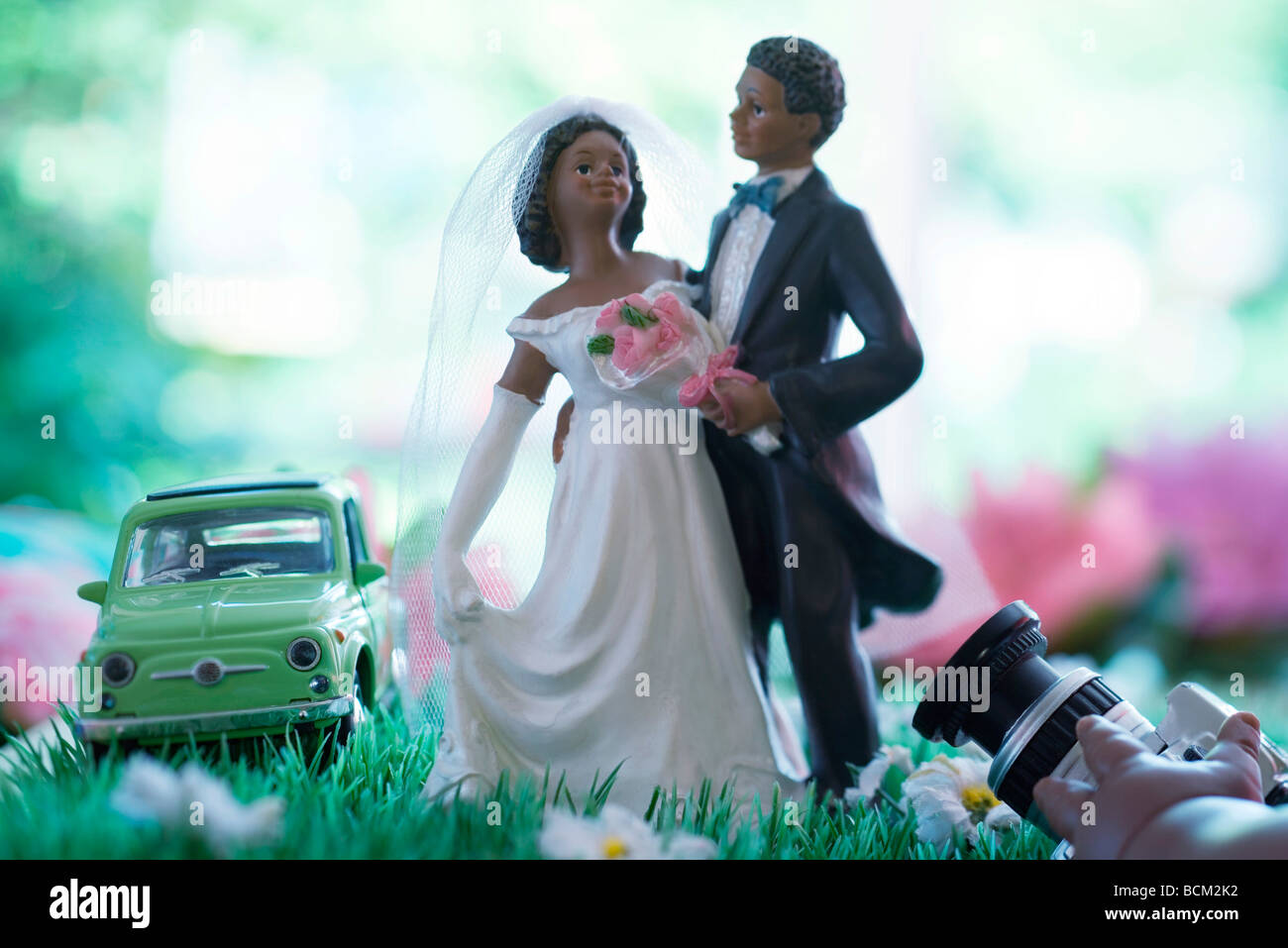 Bride and Groom figurines posant dans le champ de fleurs faux, main tenir l'appareil photo en premier plan Banque D'Images