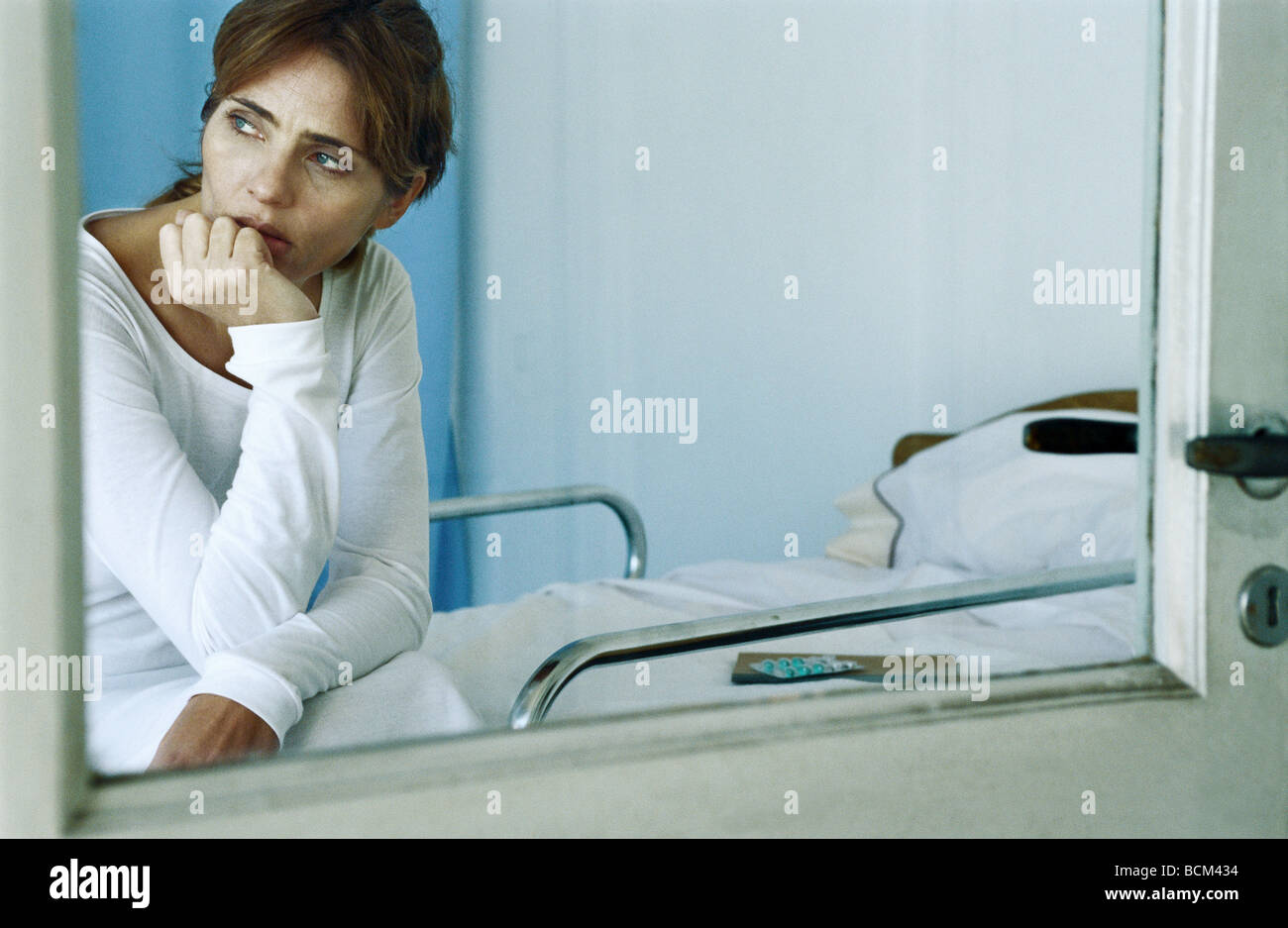Femme assise sur le lit d'hôpital, la main sous le menton, à l'écart Banque D'Images