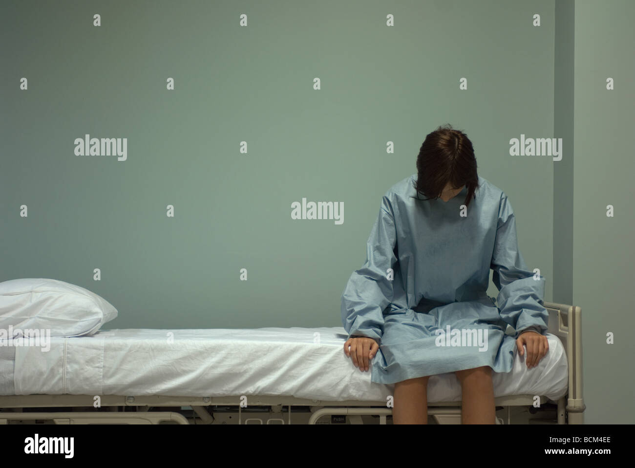 Femme assise sur lit d'hôpital, la tête en bas Banque D'Images