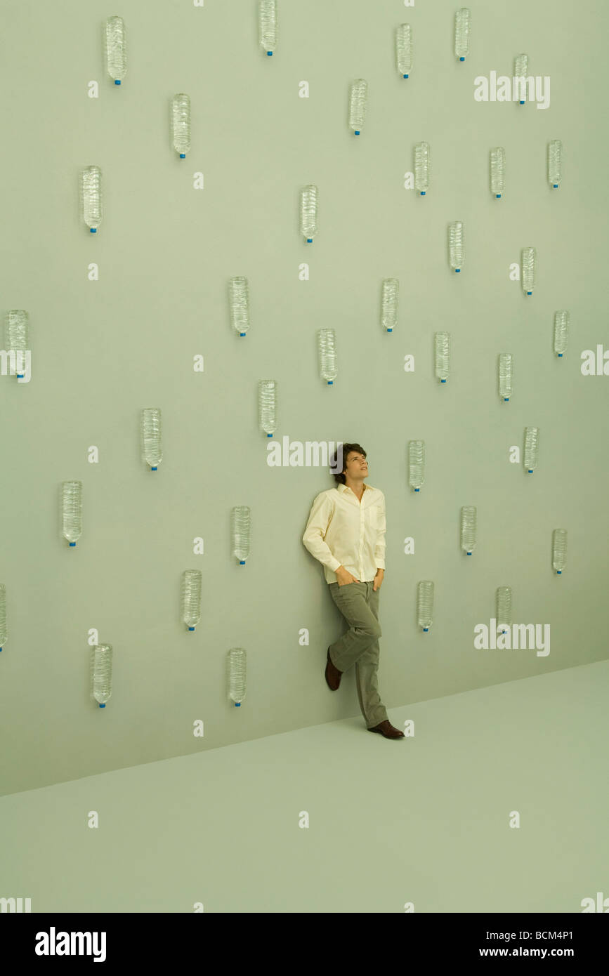 Man leaning against wall, bouteilles d'eau pleuvent autour de lui Banque D'Images
