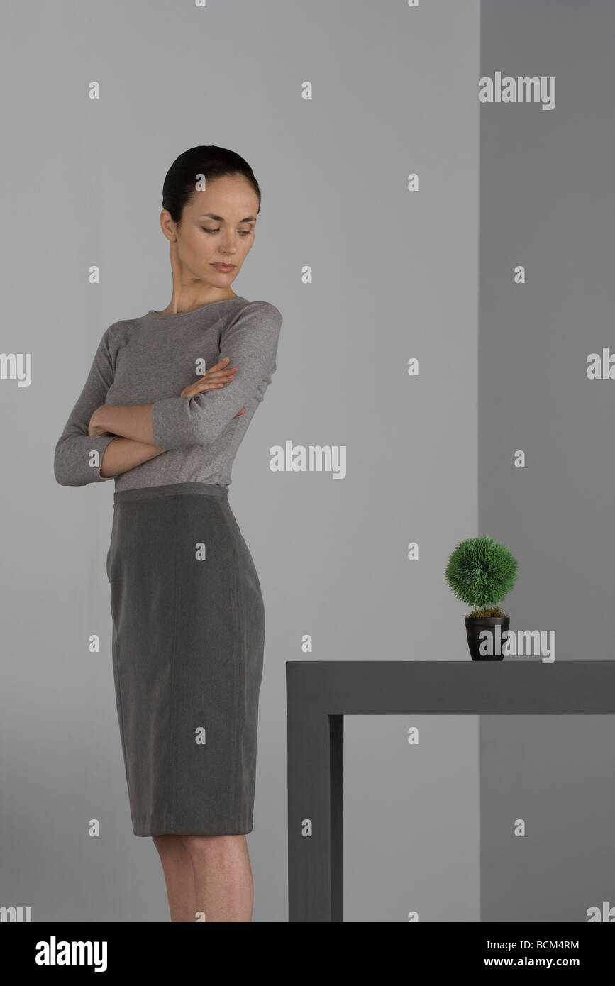 Femme debout à côté de table avec bras croisés, plante en pot Banque D'Images