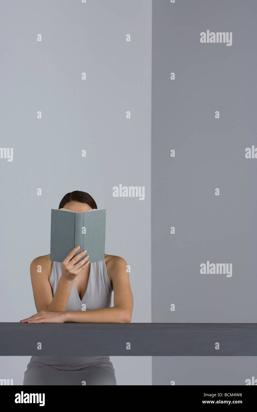 Woman sitting at table lecture, le visage masqué par d'adresses Banque D'Images