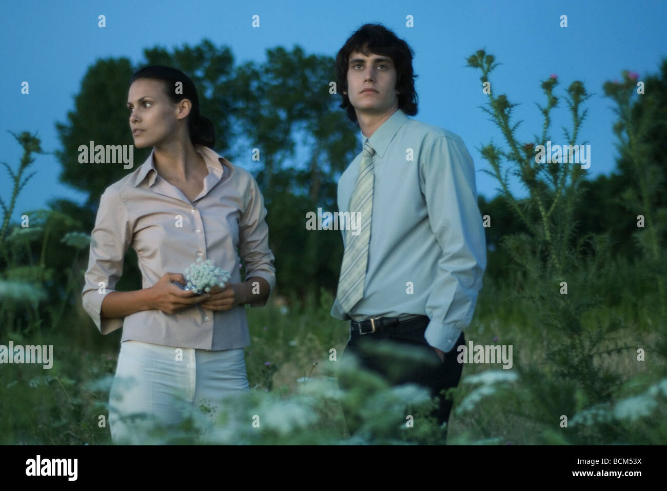 Couple standing in field, à l'écart, woman holding wildflowers Banque D'Images
