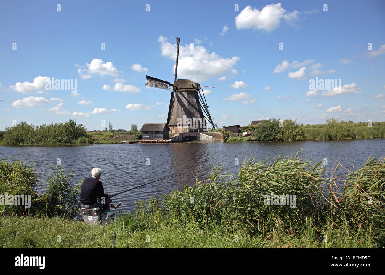 Ancien haut-wheeler moulin à Kinderdijk avec pêche pêcheur au canal Pays-bas Europe Banque D'Images