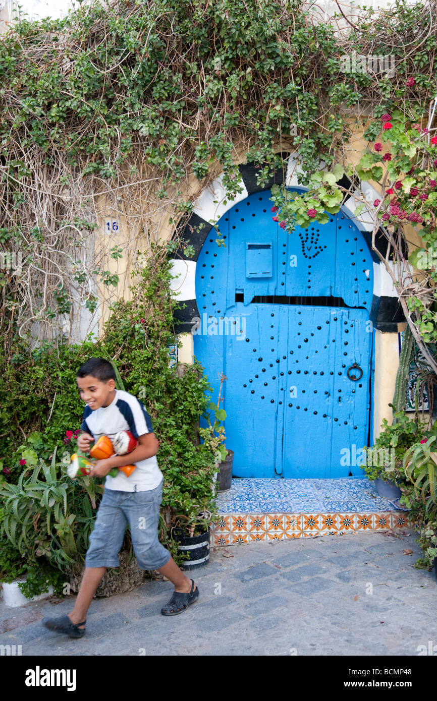 Un garçon court dans une ruelle à Sidi Bou Saïd, une charmante ville du nord de la Tunisie de murs blancs et bleus de la mer Windows & Doors Banque D'Images