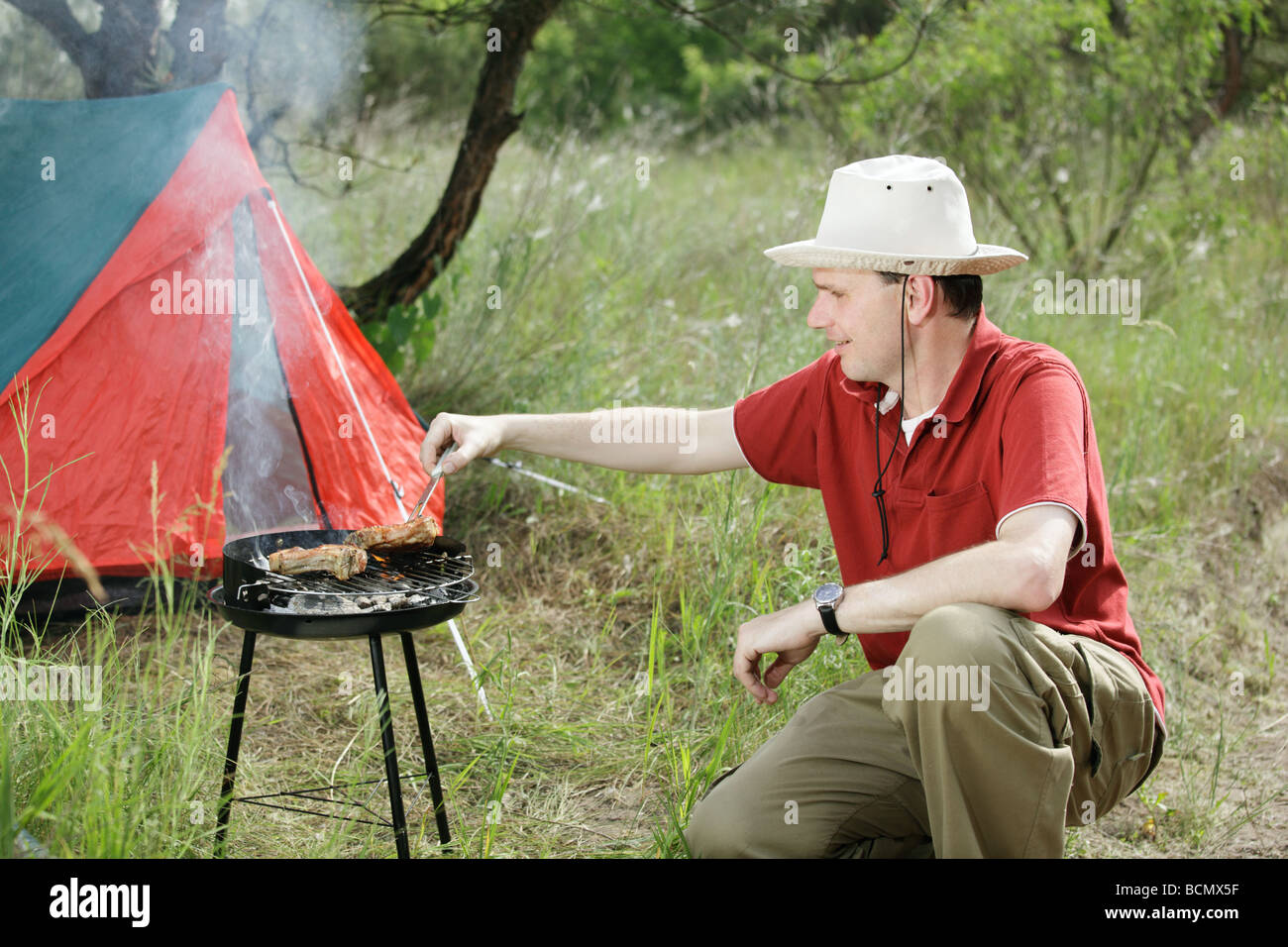 Man grilling meat en plein air près de la tente touristique Banque D'Images