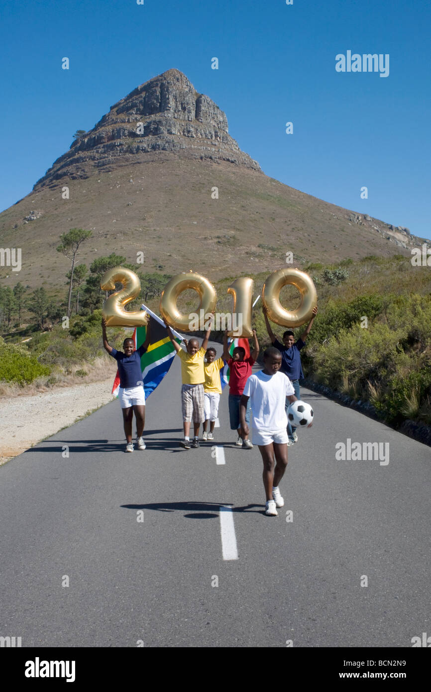 Enfants courant holding balloons façonné en chiffres 2010, avec drapeaux de l'Afrique du Sud et d'un ballon de football, les Lions Head en arrière-plan Banque D'Images