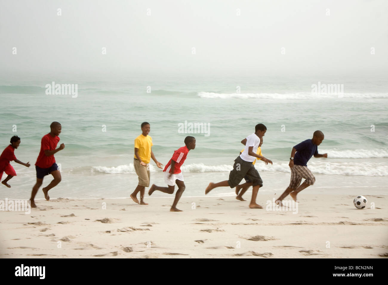 Enfants courant sur la plage à jouer au football. Blouberg Beach Banque D'Images