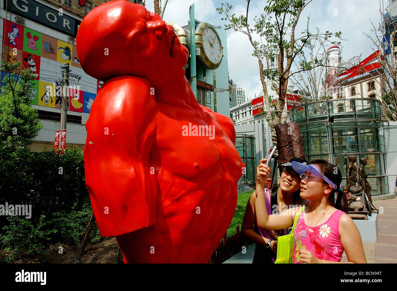 Deux jeunes woman taking photo d'une sculpture de l'homme souffrant à l'aide de téléphone mobile, Shanghai, Chine Banque D'Images