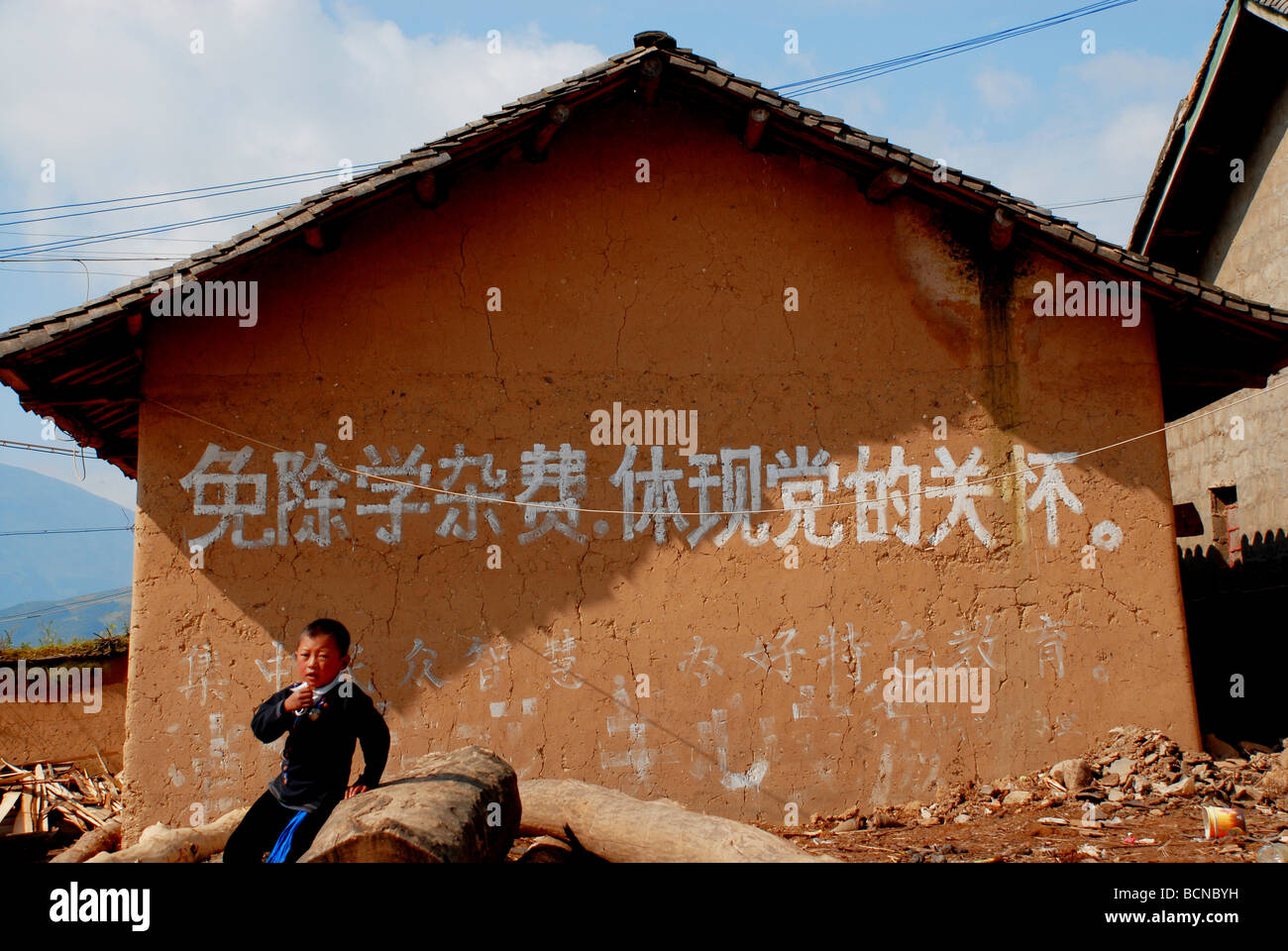 Garçon jouant devant une maison avec un slogan pour l'éducation aide financière, Ürümqi Préfecture autonome Yi, province du Sichuan, Banque D'Images