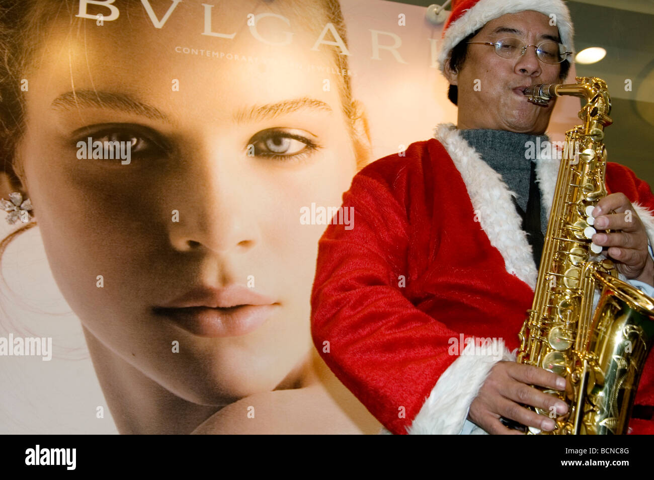 L'homme chinois dans le costume de Père Noël à jouer du saxophone dans le centre commercial avant de grande annonce de Bvlgari, Shanghai, Chine Banque D'Images