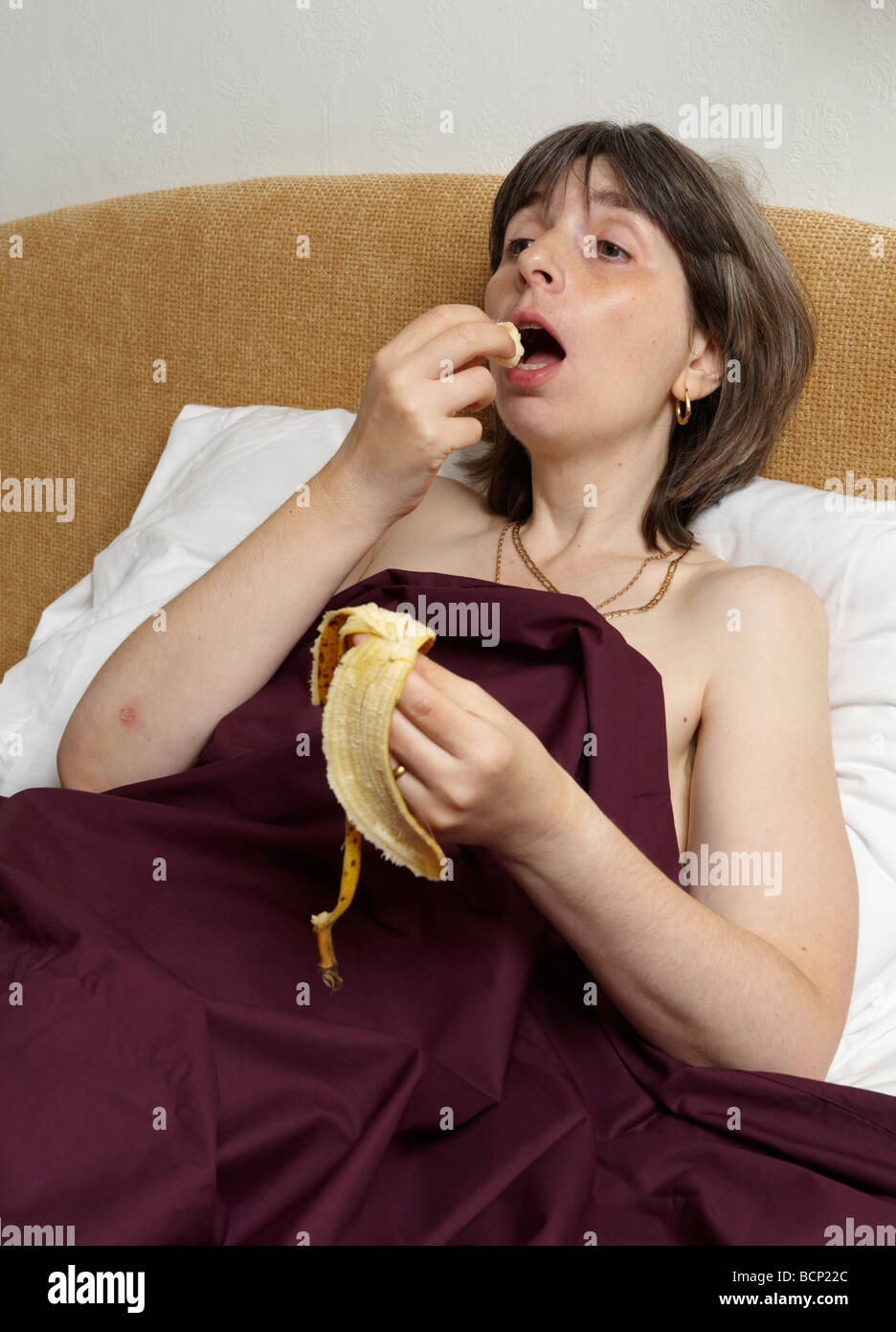 Middle aged woman eating banana suggestivement Lying in Bed Banque D'Images