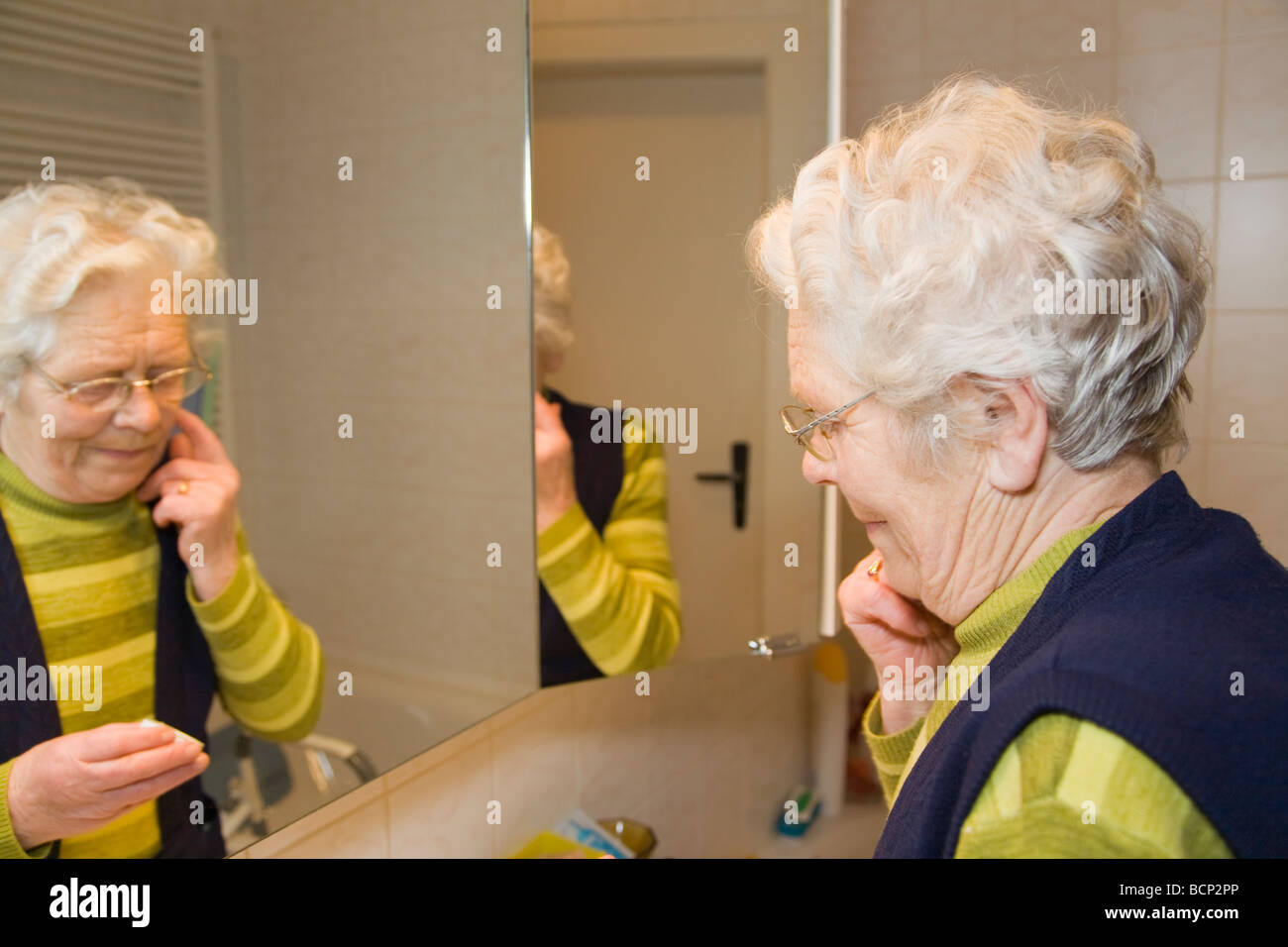 Frau dans Siebzigern cremt ihren sich das Gesicht ein Banque D'Images