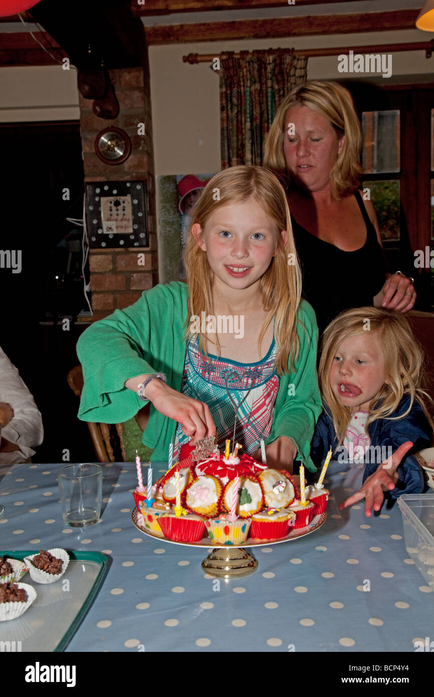 Neuf ans, fille avec gâteau d'anniversaire et affamés plus jeune soeur Cotswolds UK Banque D'Images