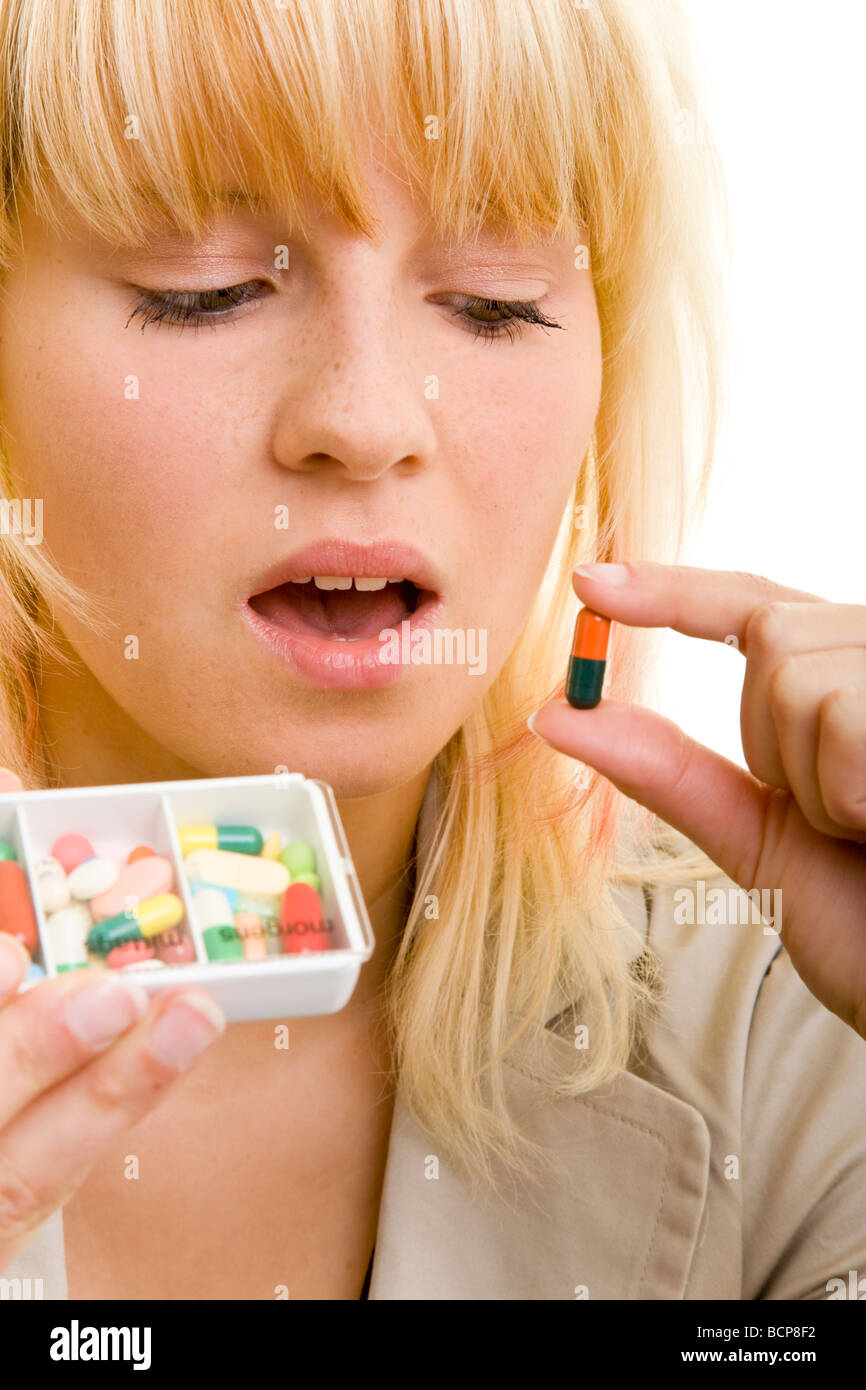 Junge Frau mit einer Pillendose in der Hand schaut eine bunte Kapsel unsicher un Banque D'Images