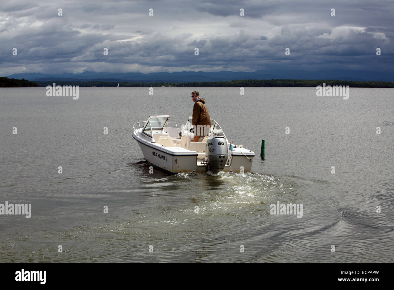 Un jeune homme sortir son bateau à moteur runabout de 17 pieds. La scène est le lac Champlain avec les montagnes Vertes du Vermont. Banque D'Images