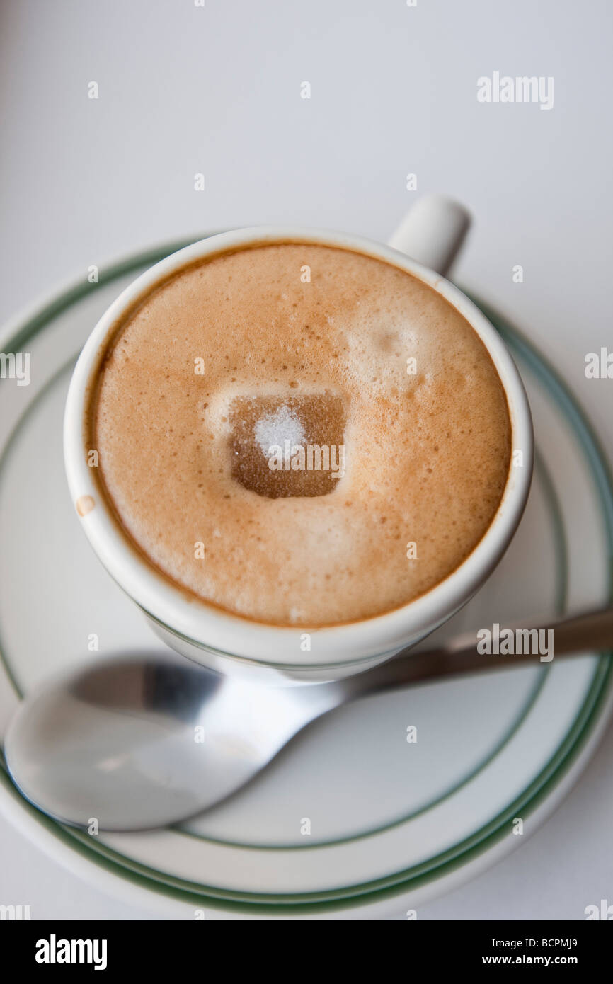 Vue de dessus d'un cube de sucre fondre dans la mousse d'un café expresso chaud boire dans une tasse avec une cuillère en métal Banque D'Images