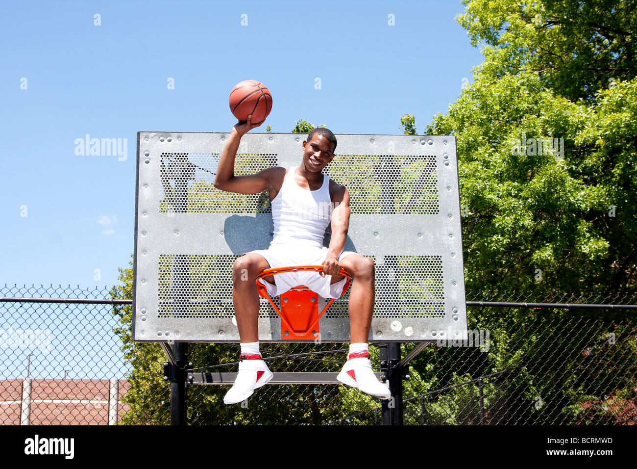 Happy smiling handsome sporty African American male basketball player vêtue de blanc et tenant sa balle avec une part Banque D'Images