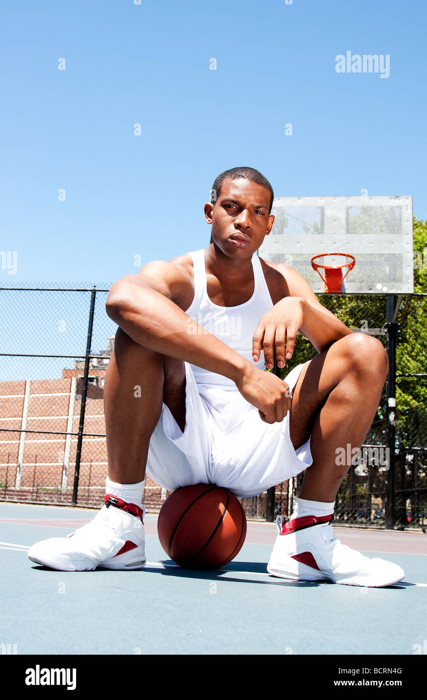 African American male sportif beau joueur de basket-ball avec l'attitude de blanc vêtue assise sur son ballon piscine en été Banque D'Images