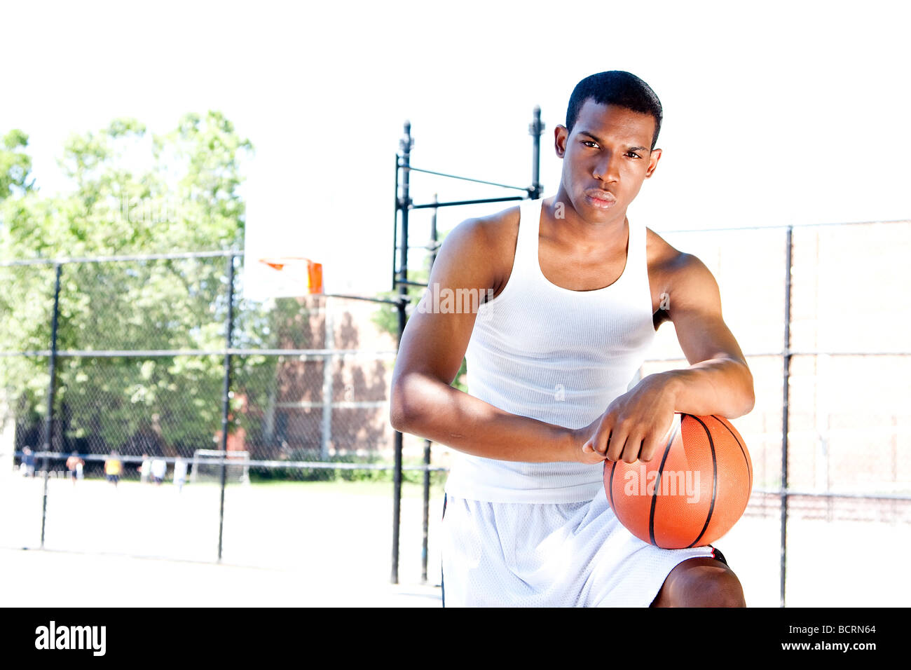 African American male sportif beau joueur de basket-ball avec attitude habillé en blanc debout avec son ballon piscine en été Banque D'Images