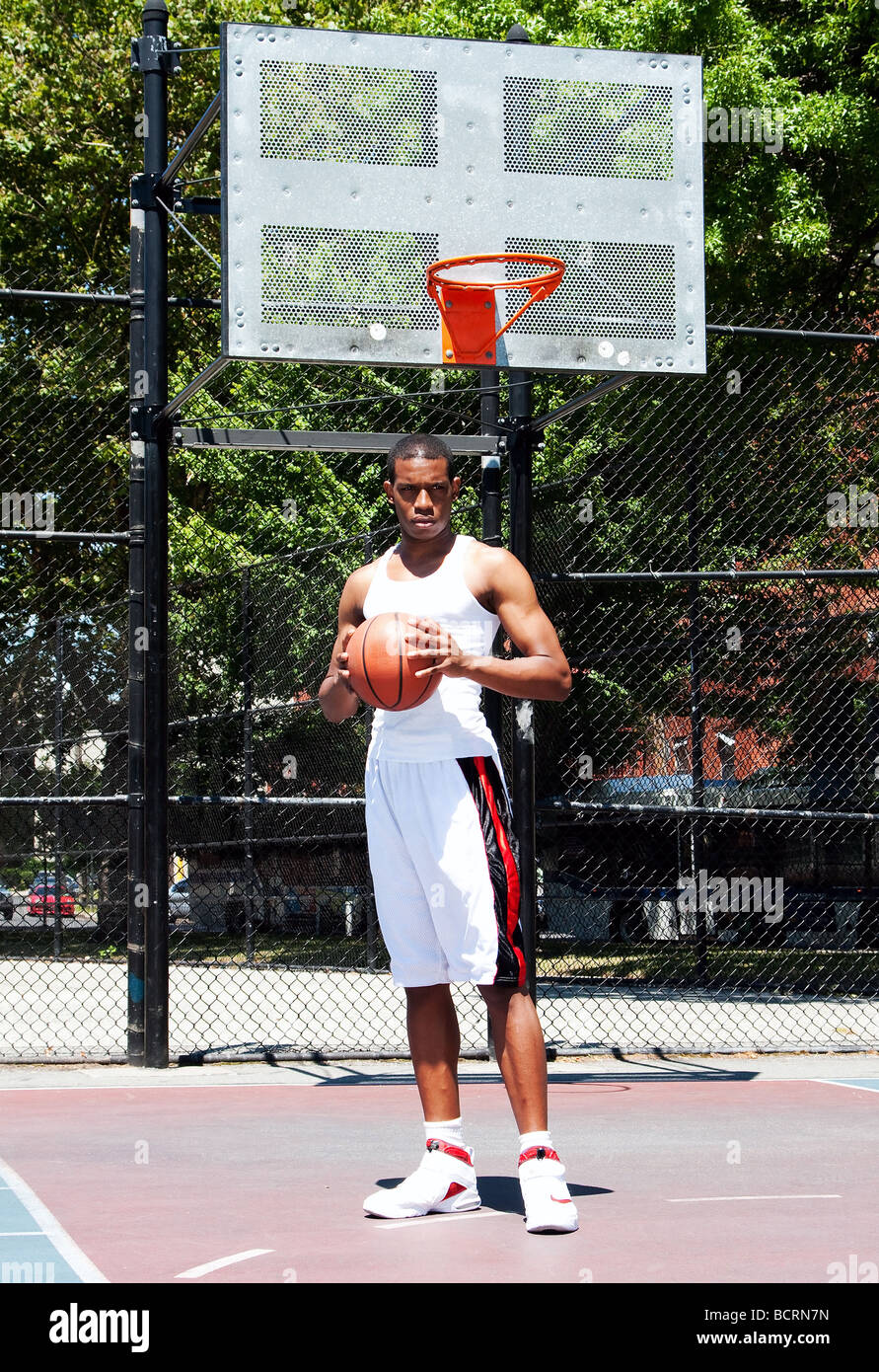 African American male sportif beau joueur de basket-ball avec attitude habillé en blanc debout tenant son ballon à deux mains Banque D'Images