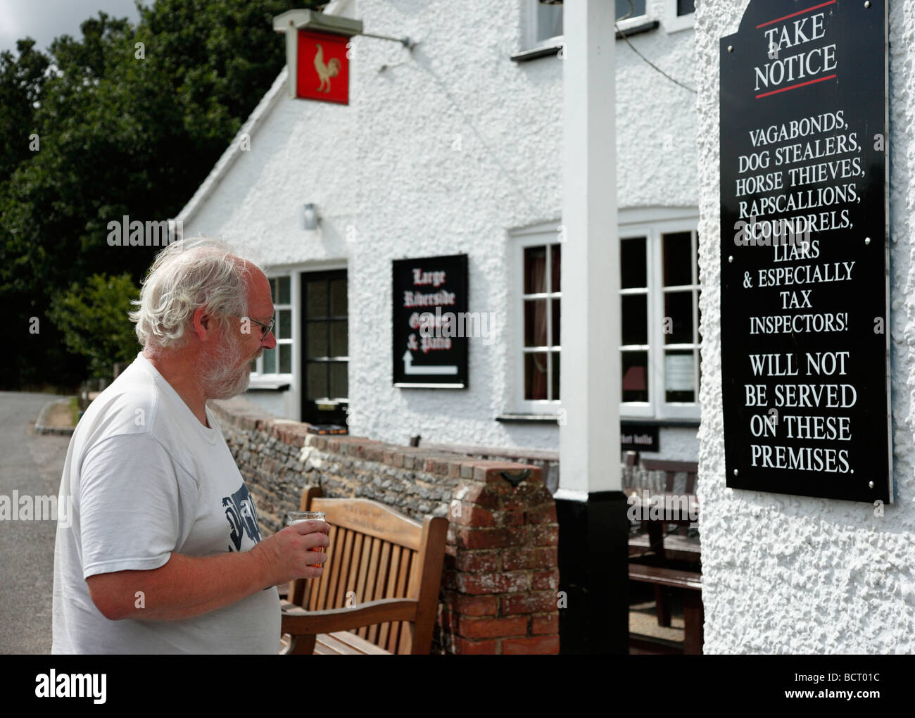 La lecture d'un homme à l'extérieur de l'avis amusant Barley Mow public house, Tilford, Surrey, Angleterre, Royaume-Uni. Banque D'Images