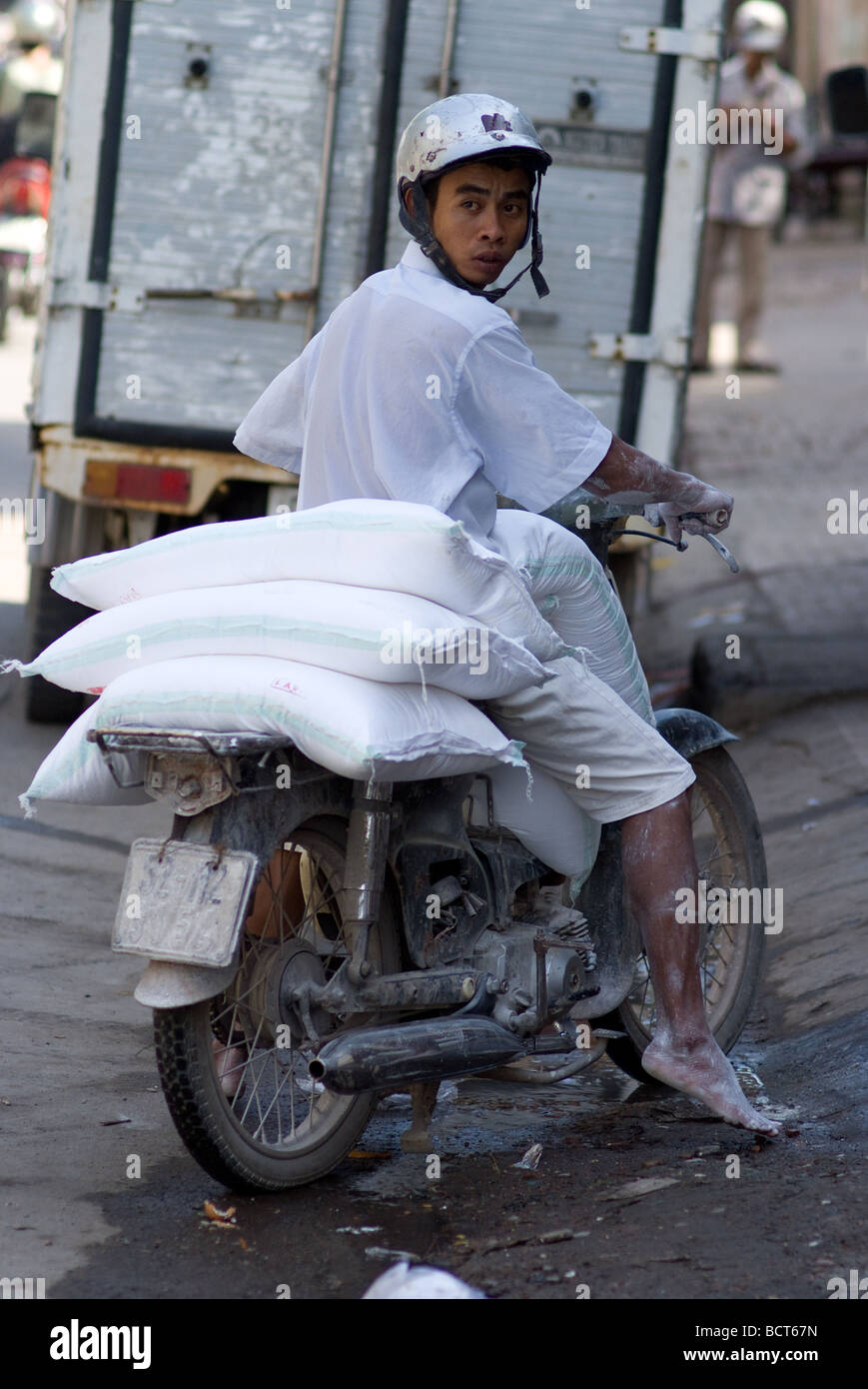 Jeune homme aux pieds nus transportant des sacs de farine sur sa moto dans le quartier chinois de Cho Lon de Ho Chi Minh Ville Vietnam Banque D'Images