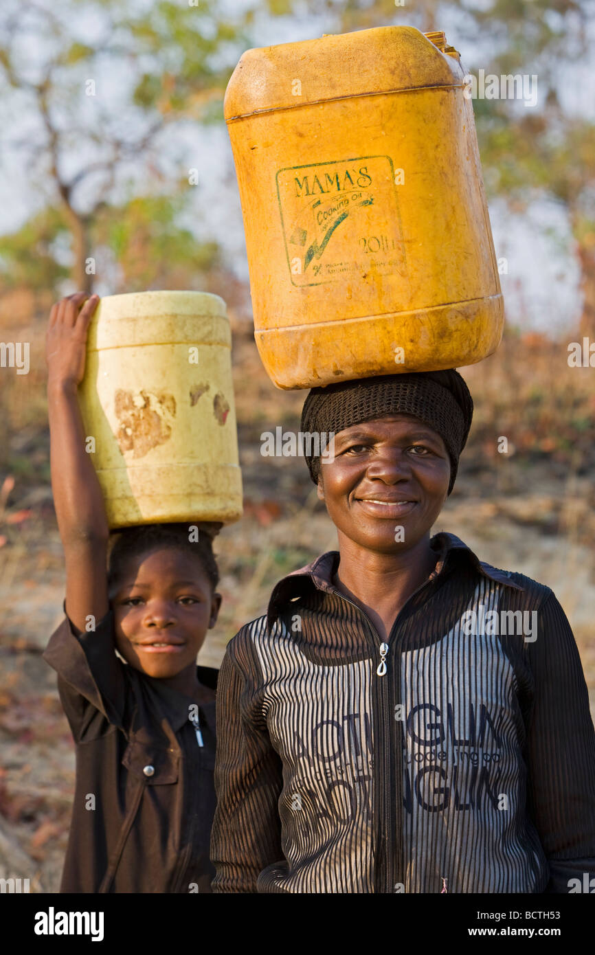 Les femmes et enfants transportant de l'eau potable dans des contenants en plastique sur la tête, la Zambie, l'Afrique Banque D'Images