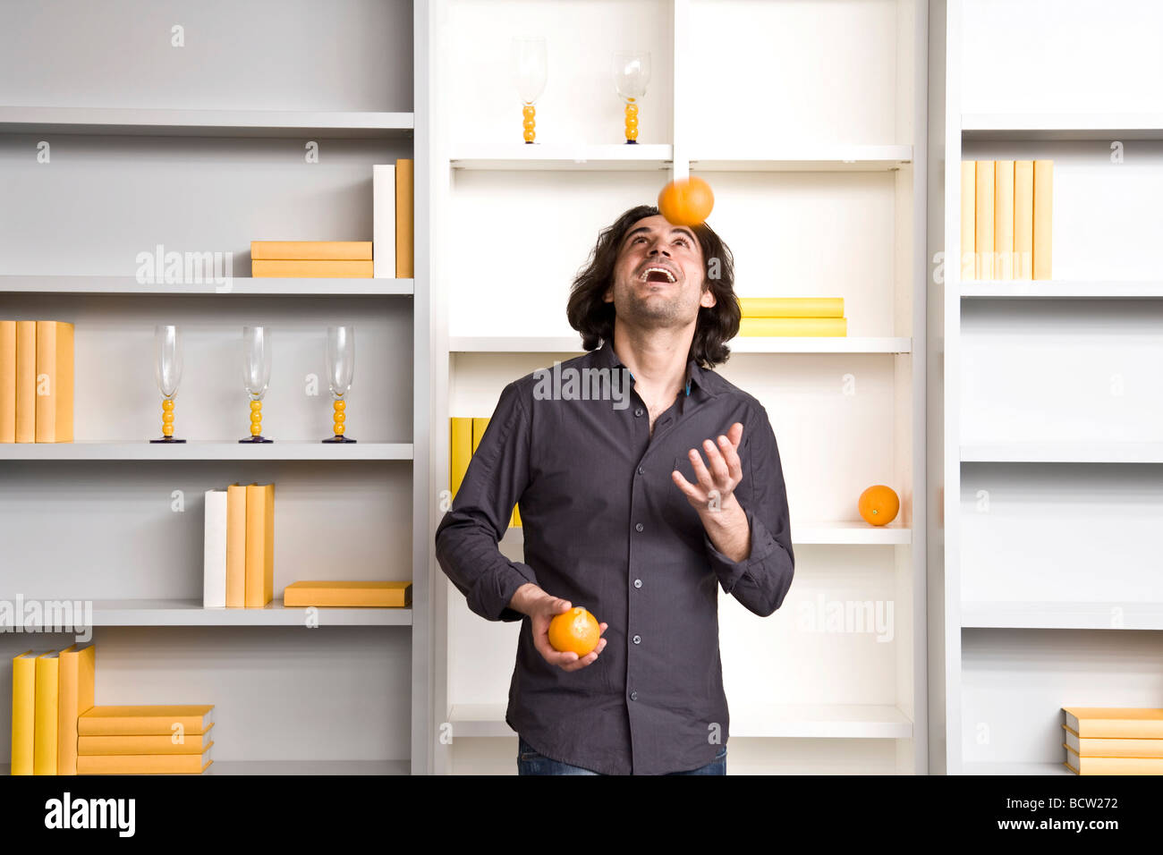 Jeune homme juggling devant une étagère d'un télévision Banque D'Images