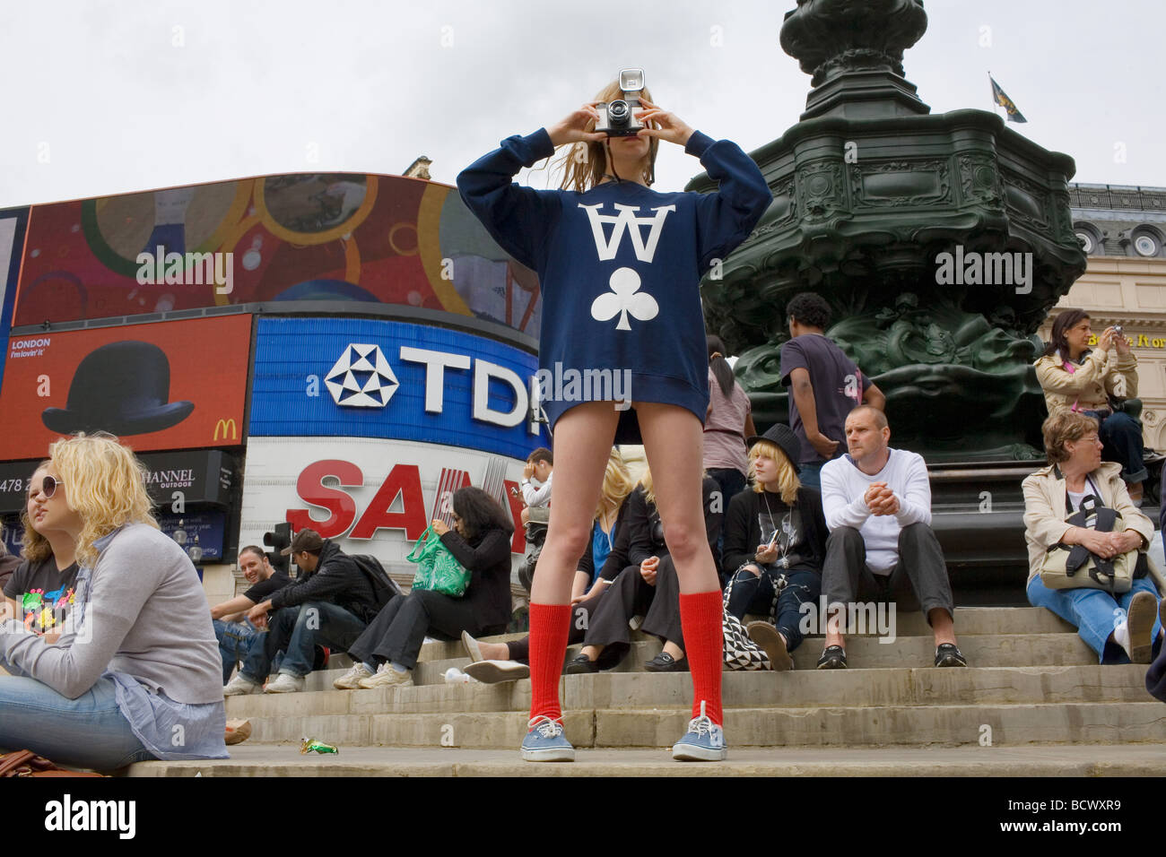 Une jeune femme blonde dans un bref retour en haut et red socks photos Piccadilly Circus par la célèbre statue d'Eros Banque D'Images