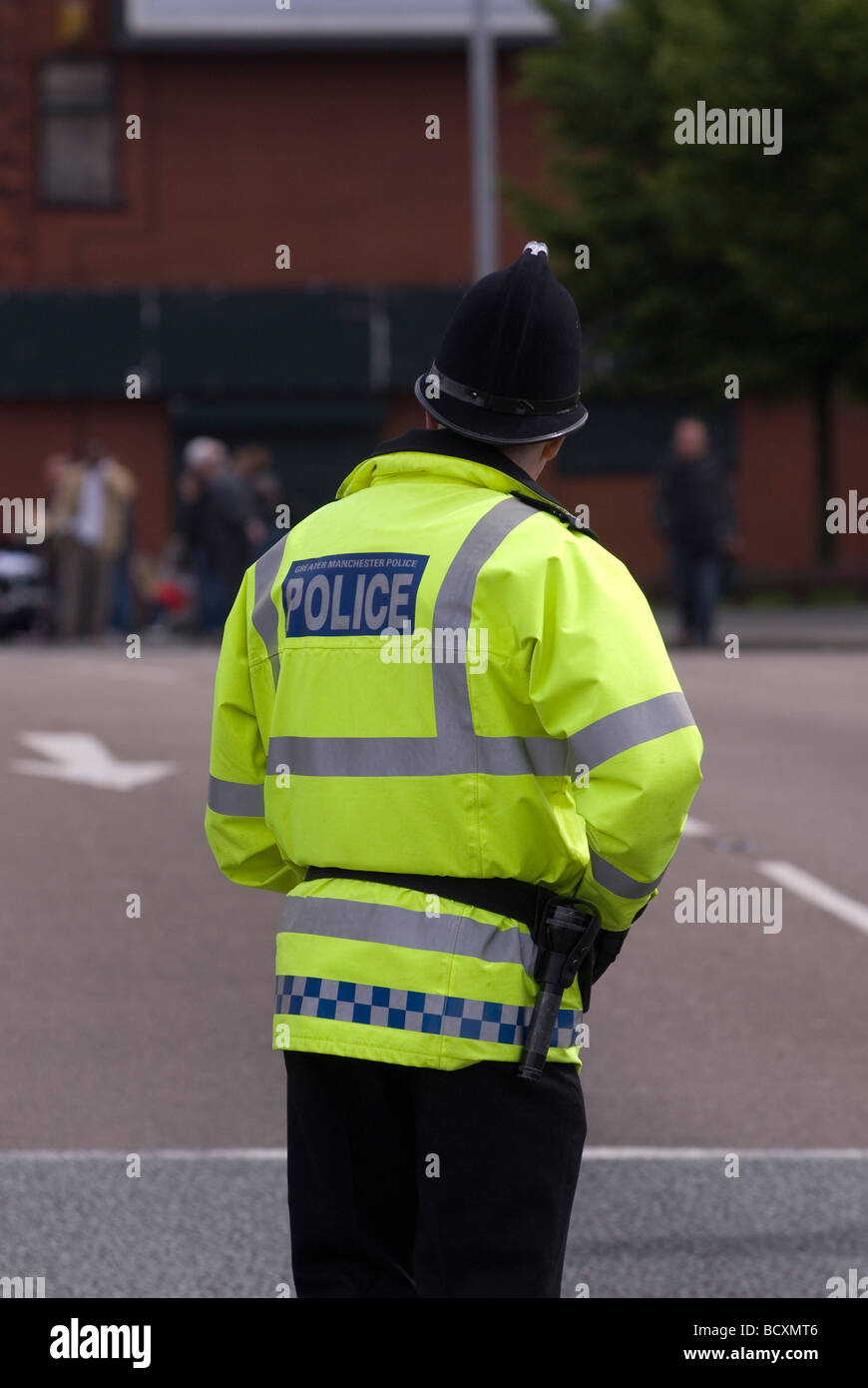 Policier dans la rue permanent regarder une foule dans la distance Manchester UK Banque D'Images