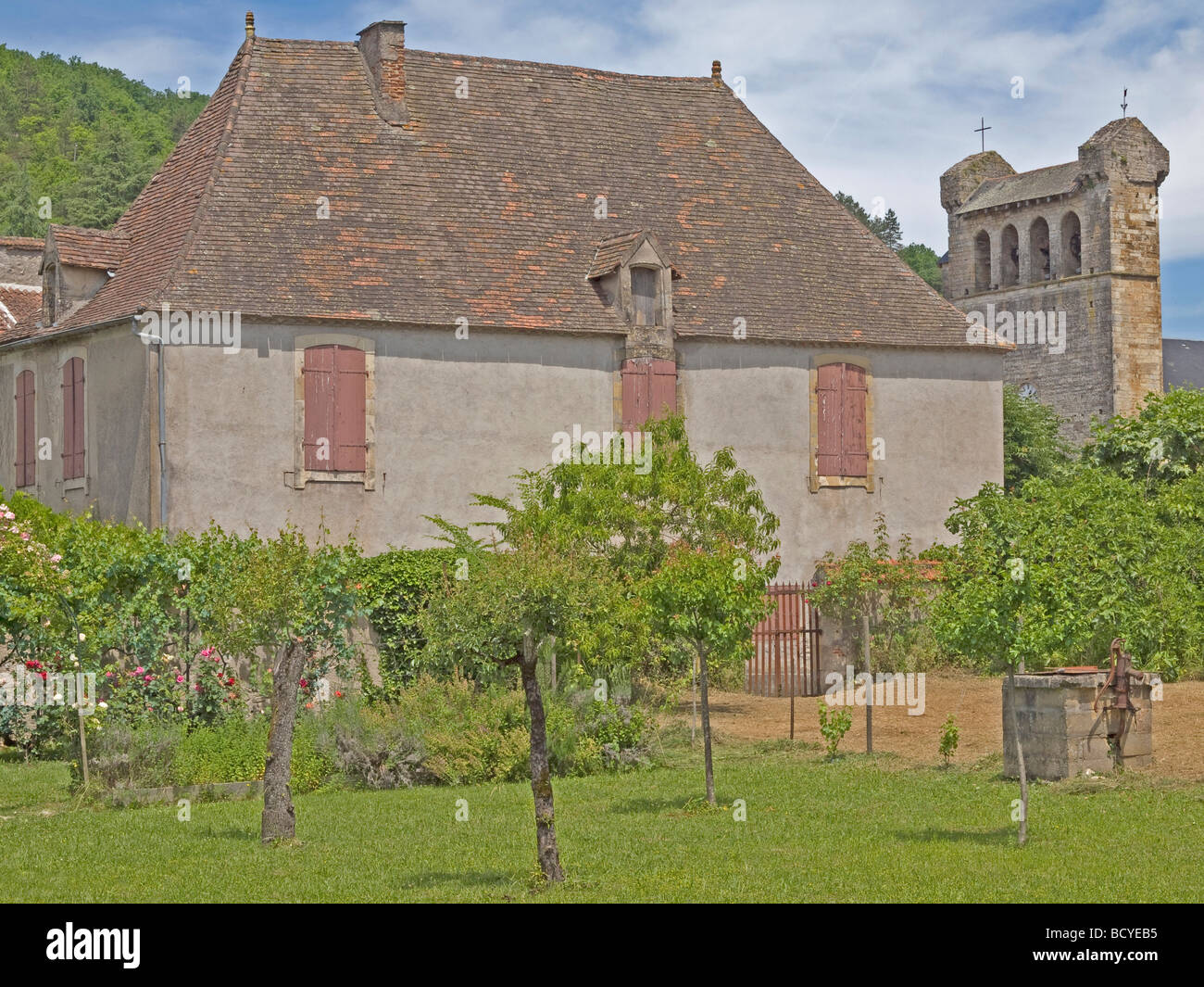 Petite maison dans jardin avec peu d'arbres et une pompe à eau en arrière-plan un clocher à Castelfranc en France Banque D'Images