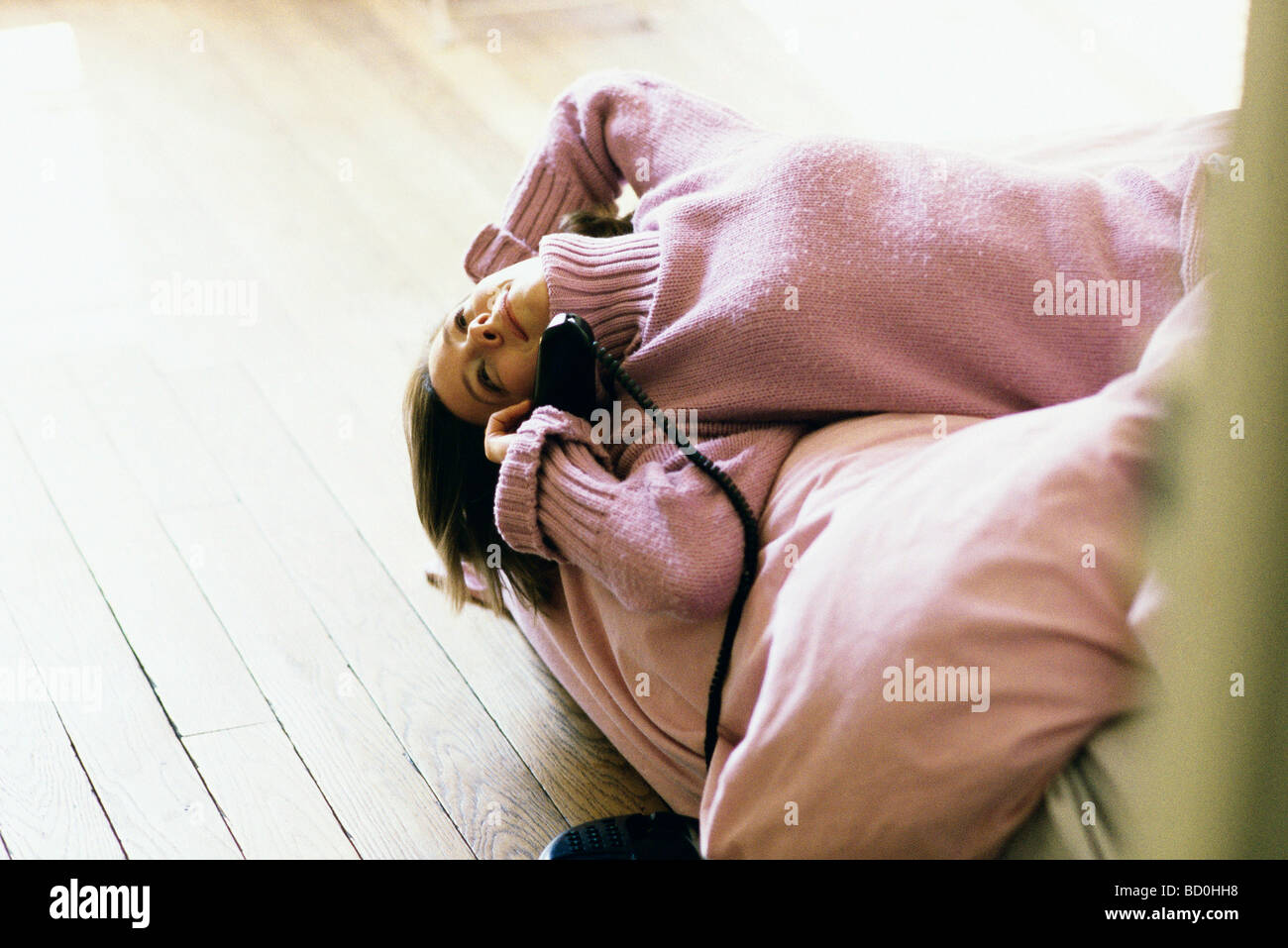 Femme couchée sur le dos sur le lit à l'aide de Phone, smiling, looking away Banque D'Images