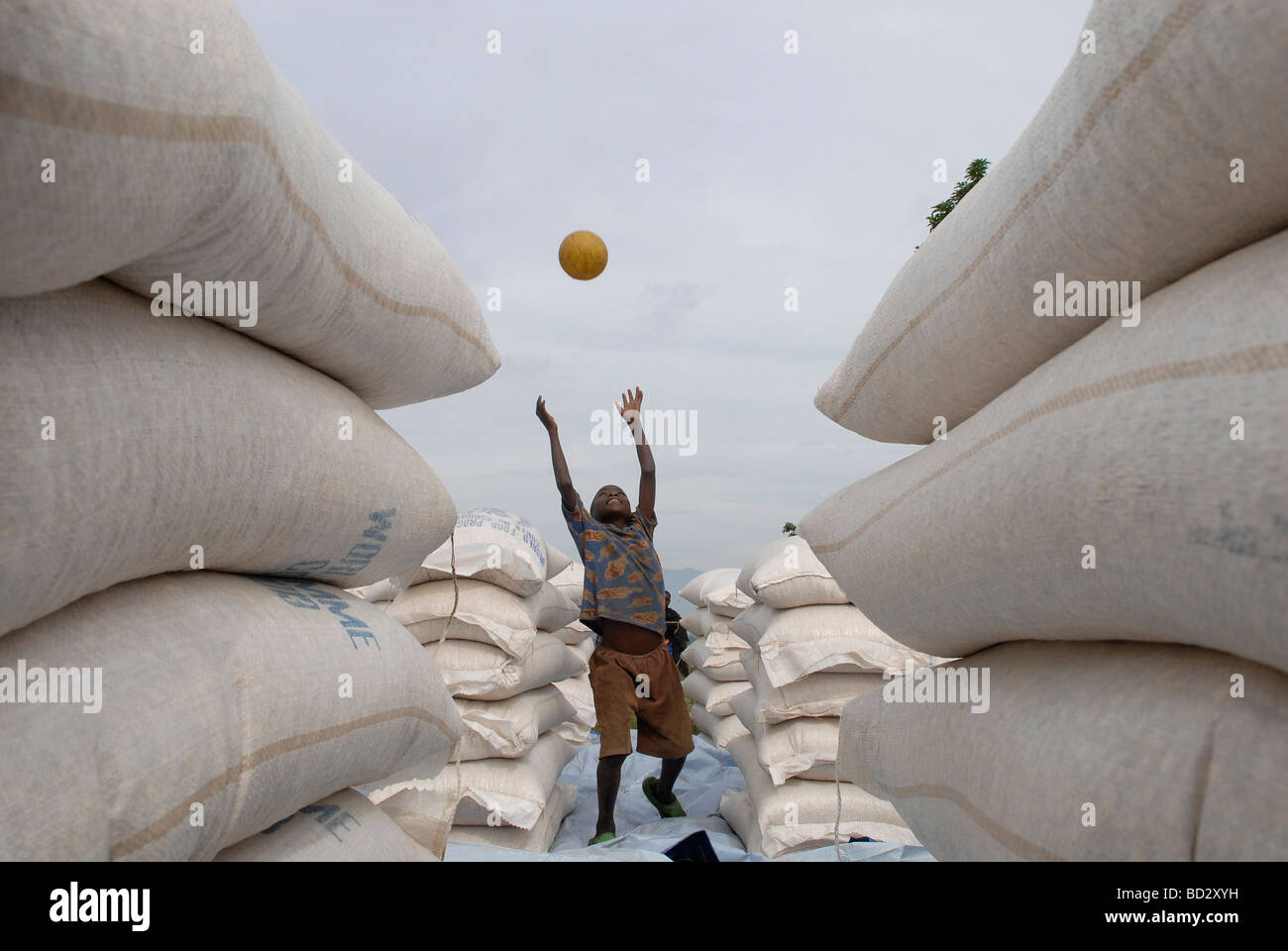 Les jeunes personnes déplacées Garçon jouant au milieu des sacs de denrées alimentaires de base à un programme alimentaire mondial LE PAM distribution point au Nord Kivu, RD Congo Banque D'Images