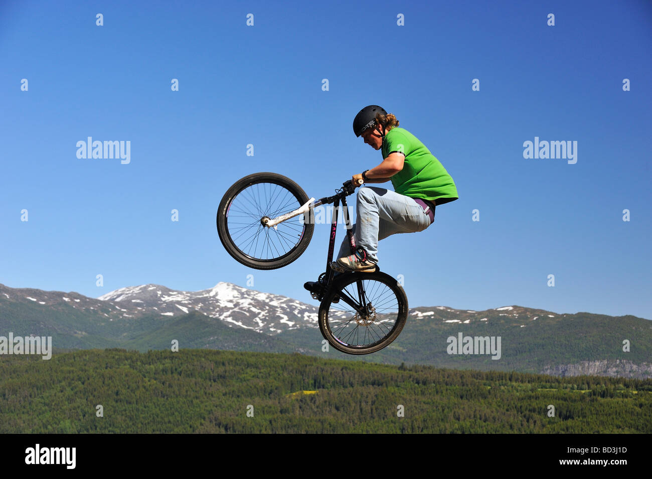 Le BMX rider volant dans les airs avec la forêt et montagne en arrière-plan Banque D'Images