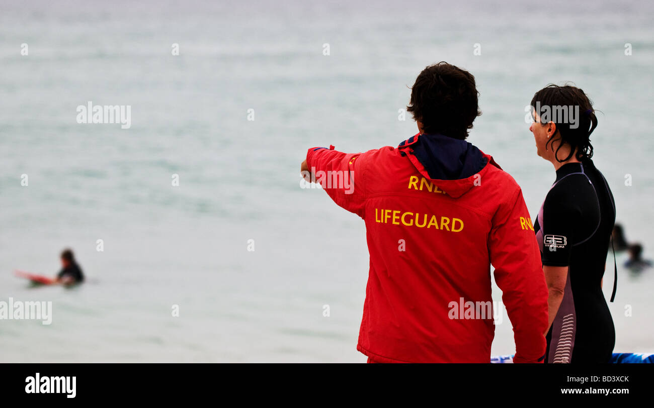 Un surfeur de parler à un sauveteur RNLI sur la plage de Sennen à Cornwall. Banque D'Images