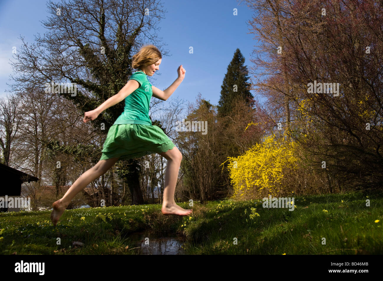 Girl jumping over creek Banque D'Images