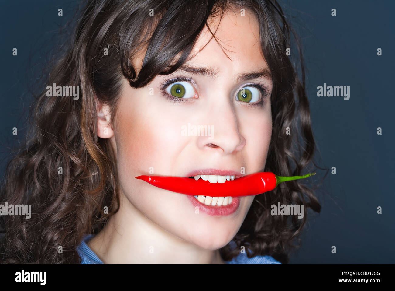 Jeune brunette woman holding chili dans sa bouche Banque D'Images