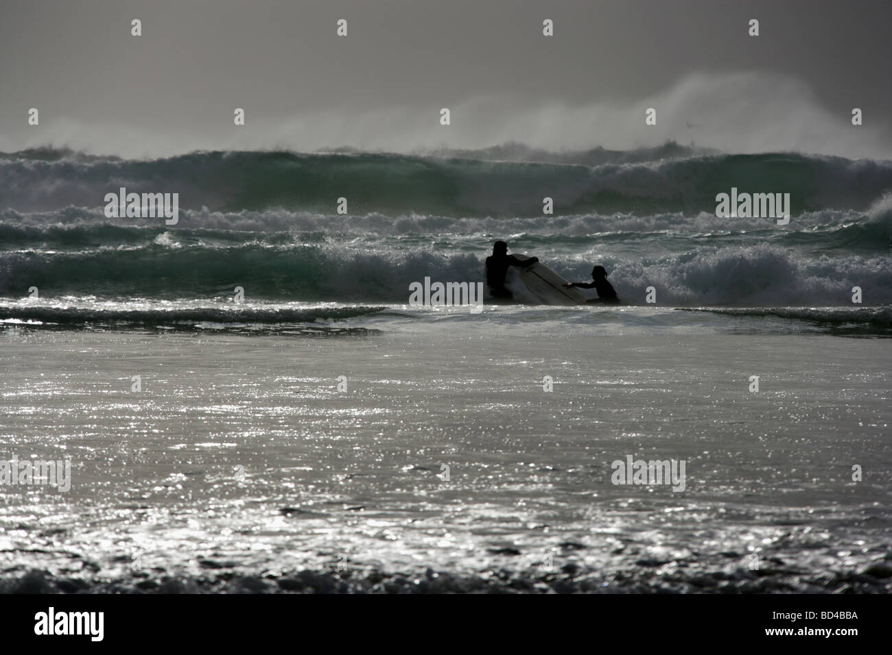 Domaine de la baie de Watergate, en Angleterre. La silhouette vue de deux surfers en utilisant la même planche de surf sur une mer agitée 24. Banque D'Images