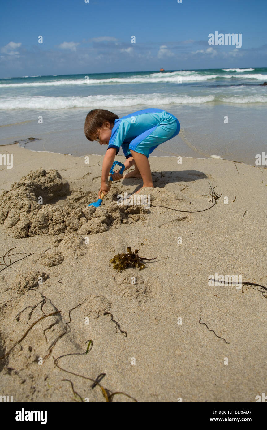 Un garçon de six ans dans un sunsuit joue dans le sable à Sennen Cove beach, Cornwall, UK Banque D'Images