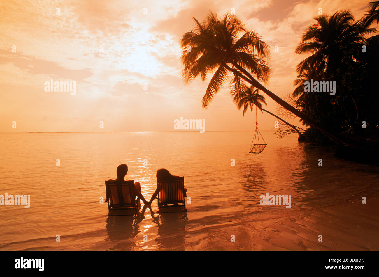 Couple assis dans des chaises de plage dans les eaux à Meeru Island aux Maldives au lever du soleil Banque D'Images