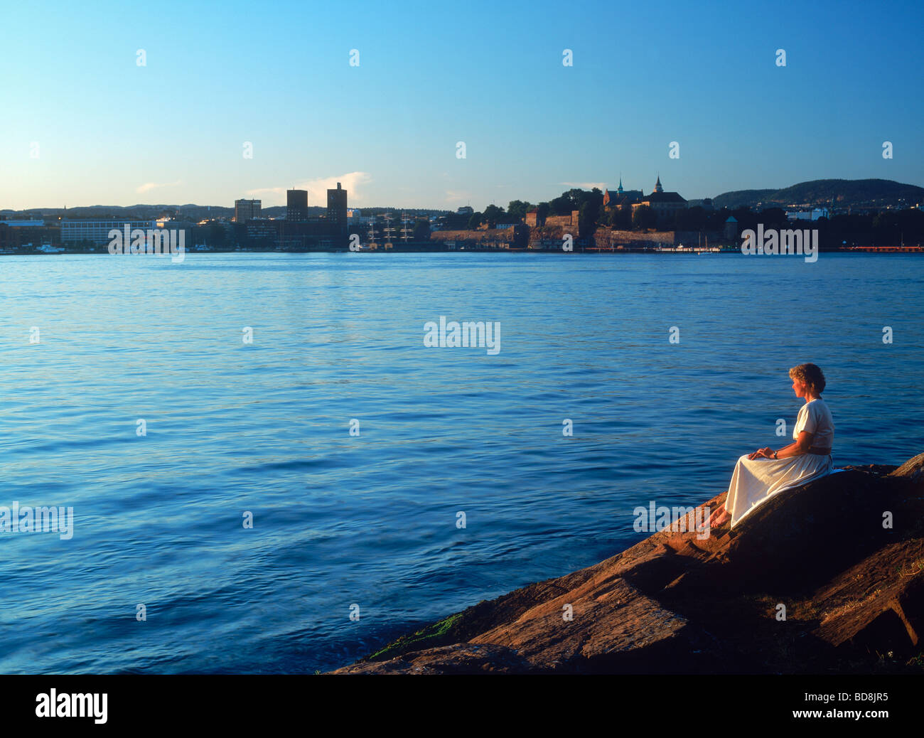 Femme assise sur un rivage rocailleux sur journée d'été romantique en face de la jetée sur le port d'Oslo Aker Banque D'Images