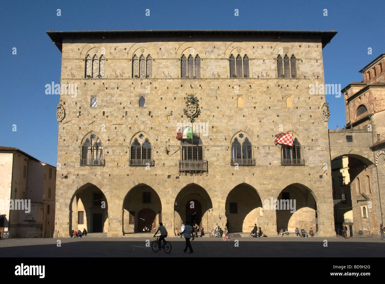 Les cyclistes passant par la piazza avec le drapeau italien en face de l'immeuble Commune médiévale à Pistoia Banque D'Images