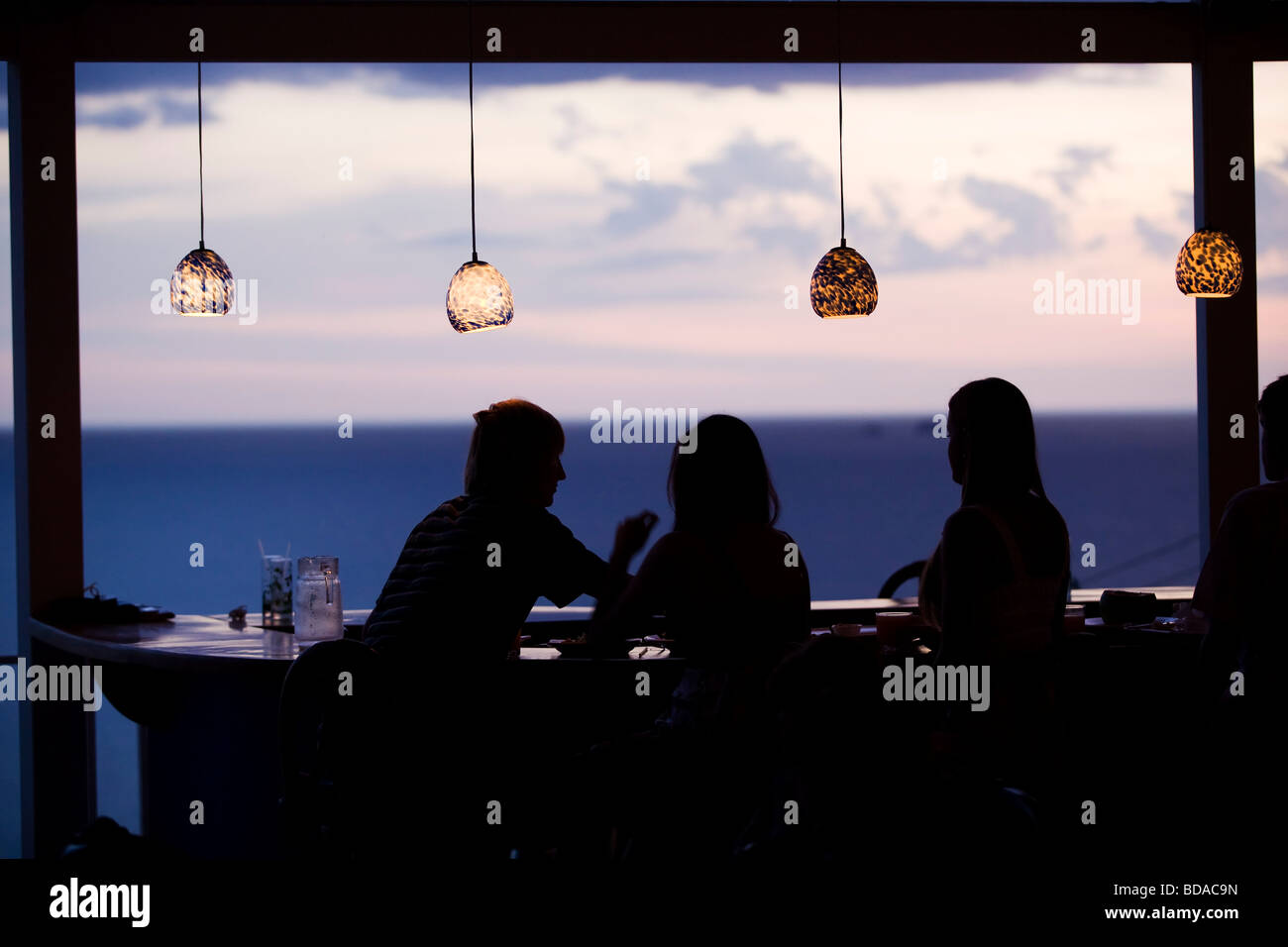 Un groupe de jeunes gens s'asseoir dans un bar au coucher du soleil. C'est crépuscule et le ciel est coloré. Au Mar y Sol à Guanacaste, Costa Rica Banque D'Images