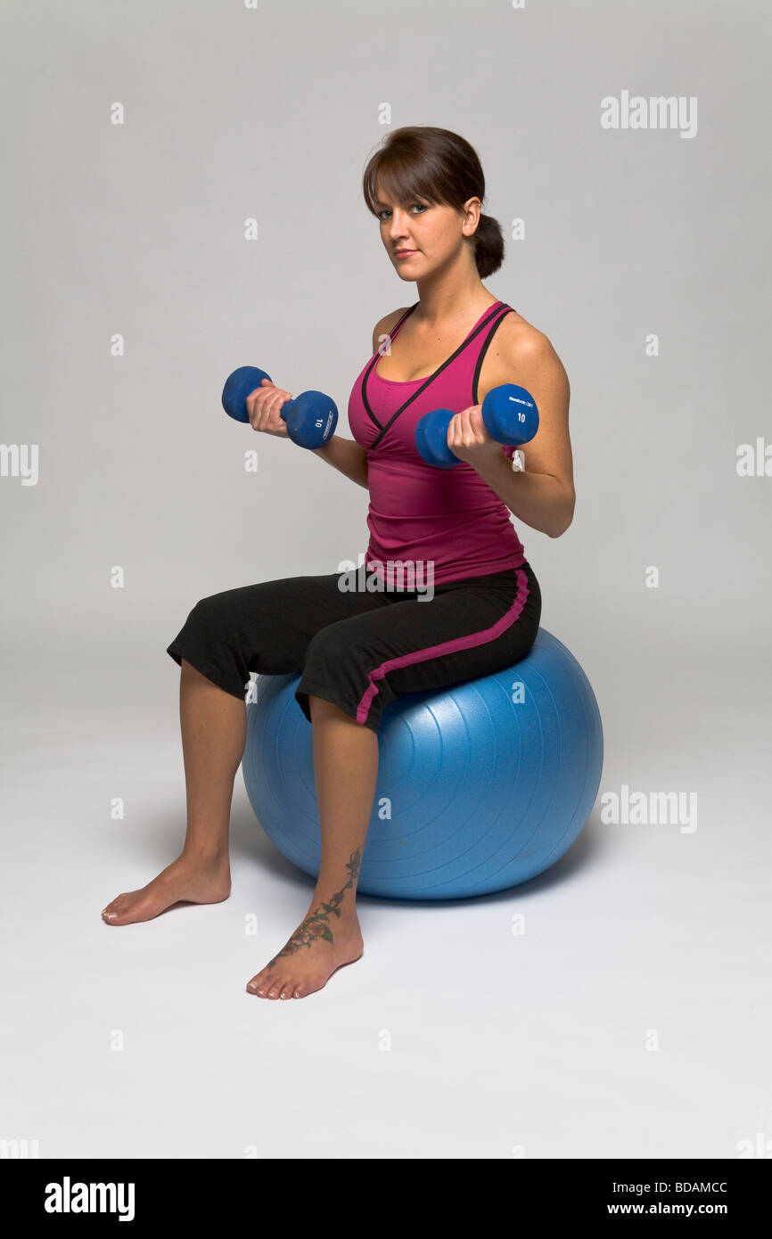 Femme assise sur une boule de forme physique faisant un double biceps de dumbell Banque D'Images