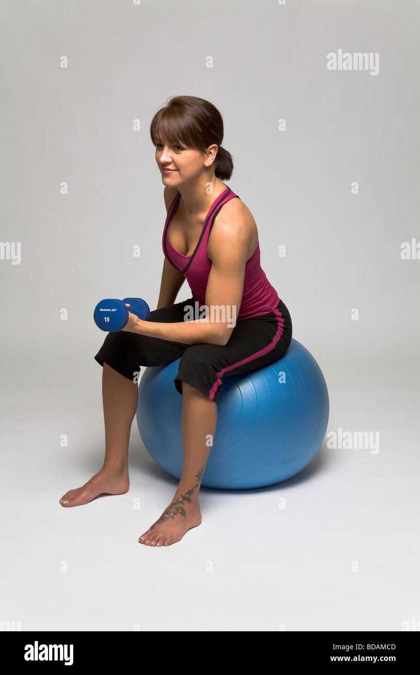 Femme assise sur une boule de forme physique de faire un seul de dumbell bicep Banque D'Images