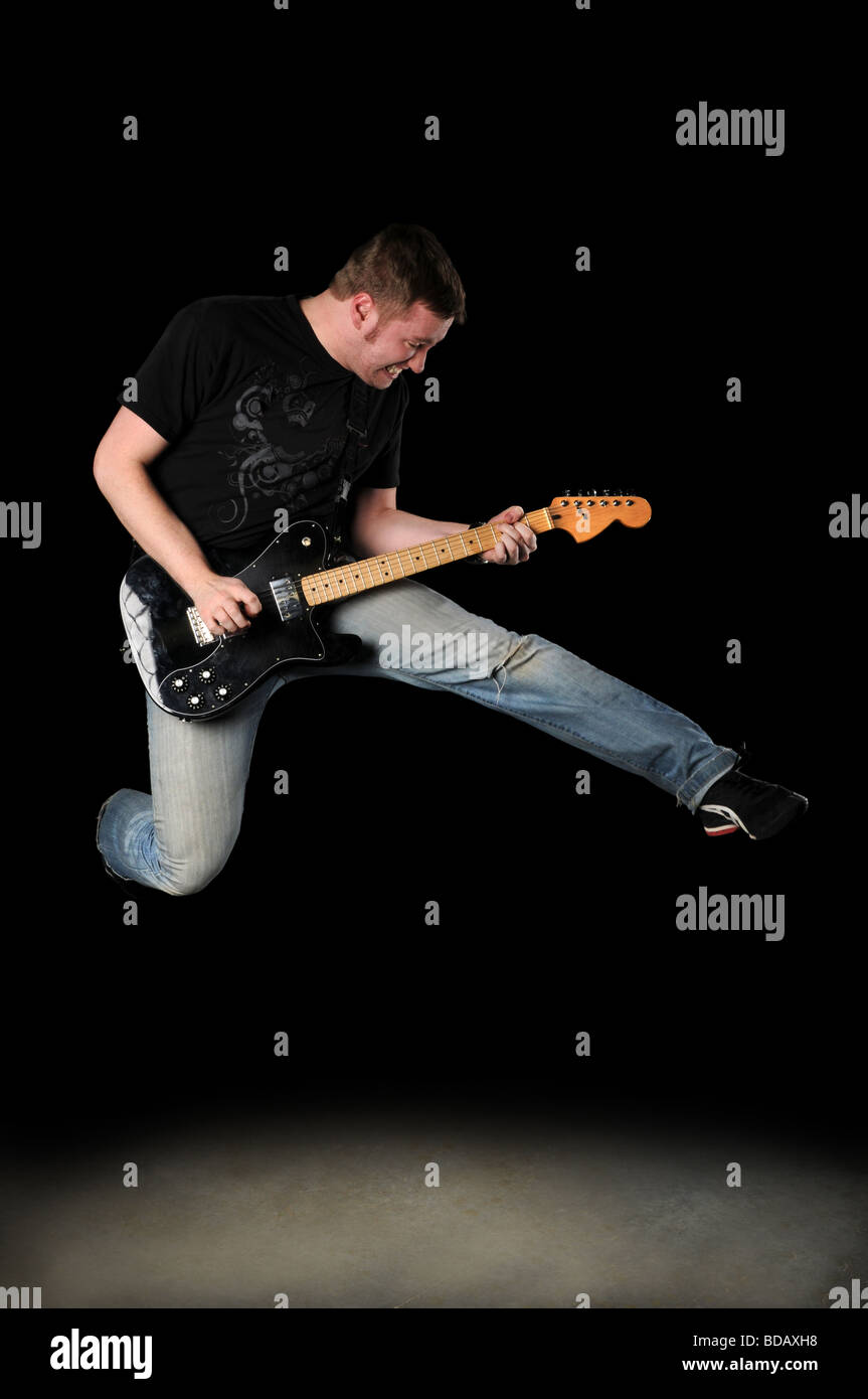 Joueur de guitare sautant par-dessus un fond sombre Banque D'Images