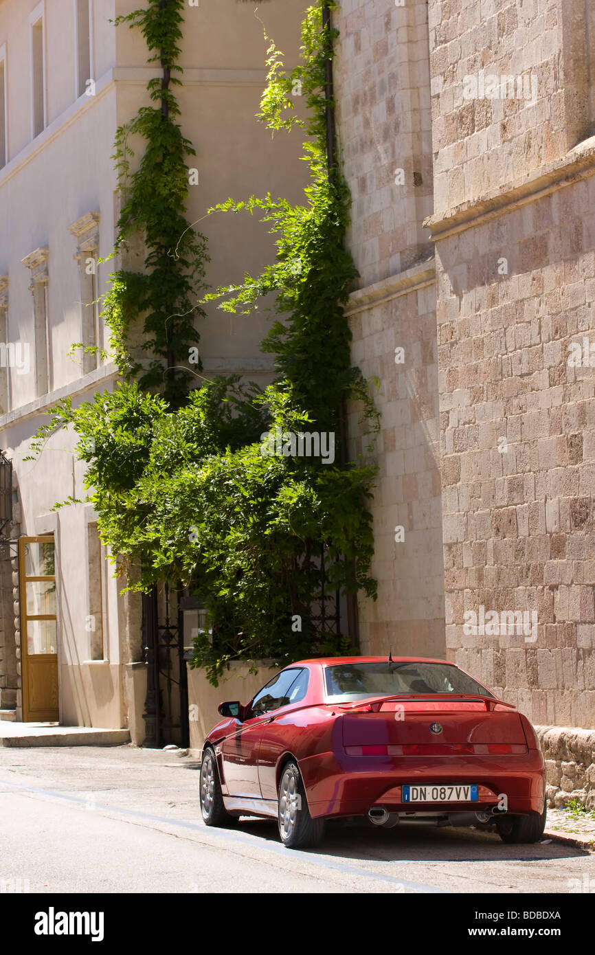 Une voiture de sport rouge garée dans une rue dans une petite ville en Italie. Alfa Romeo araignée vue de l'arrière dans une rue en Italie un après-midi ensoleillé. Banque D'Images