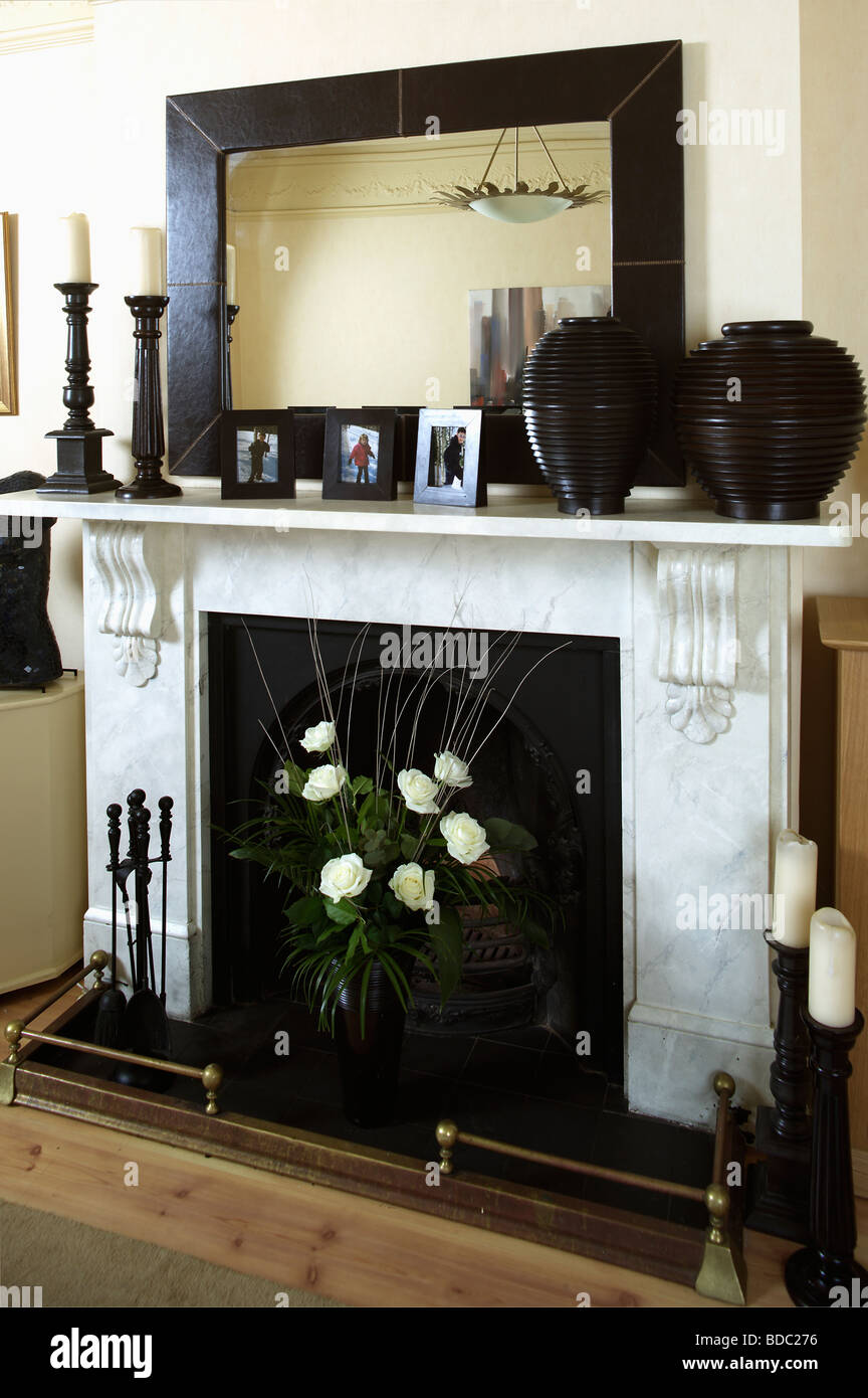 Grand miroir encadré noir rectangulaire sur la cheminée de marbre noir avec des Vases et chandeliers et vase de roses blanches dans le foyer Banque D'Images